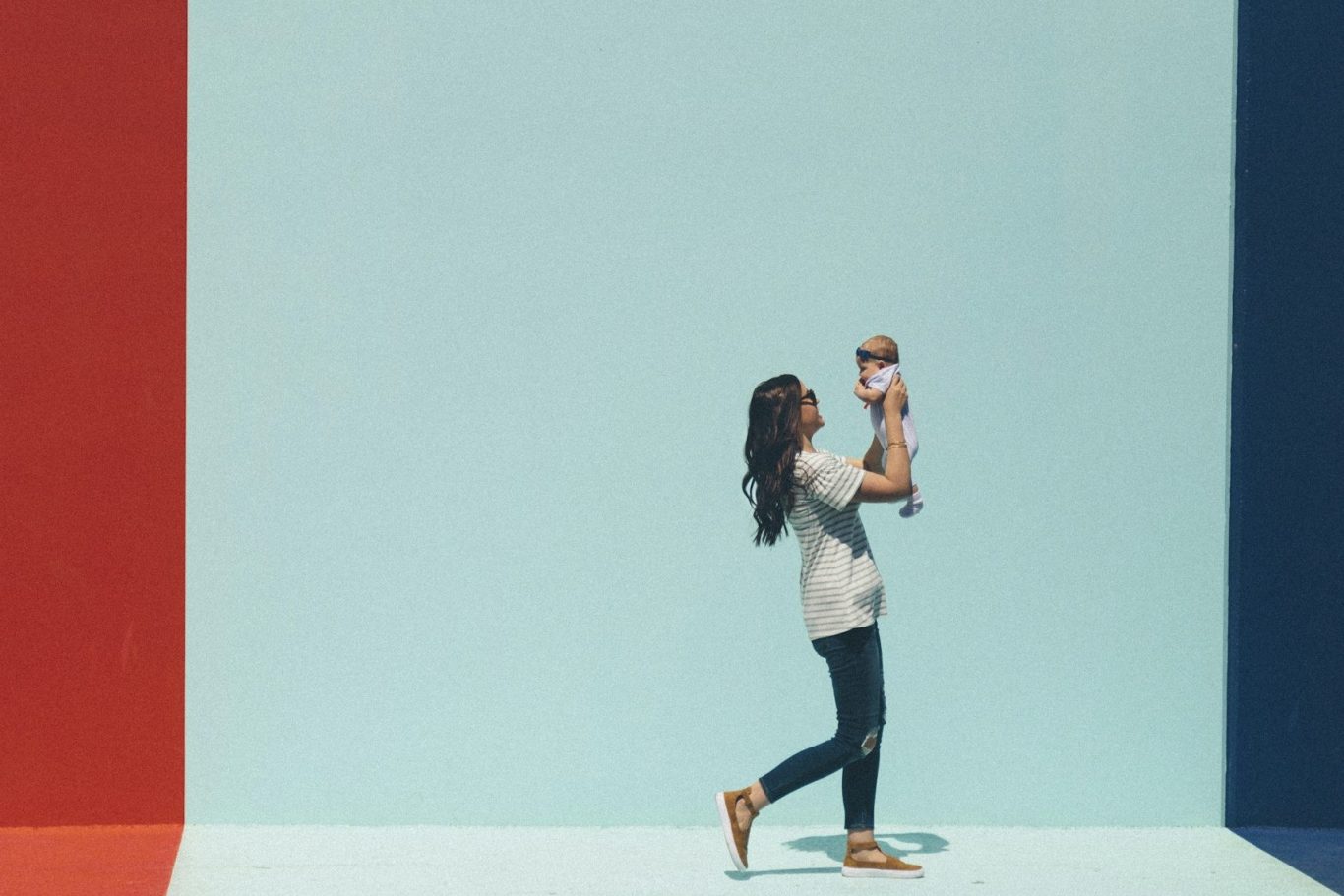 Eine Mutter hebt ihr Baby vor einer turquoisefarbenen Wand hoch.
